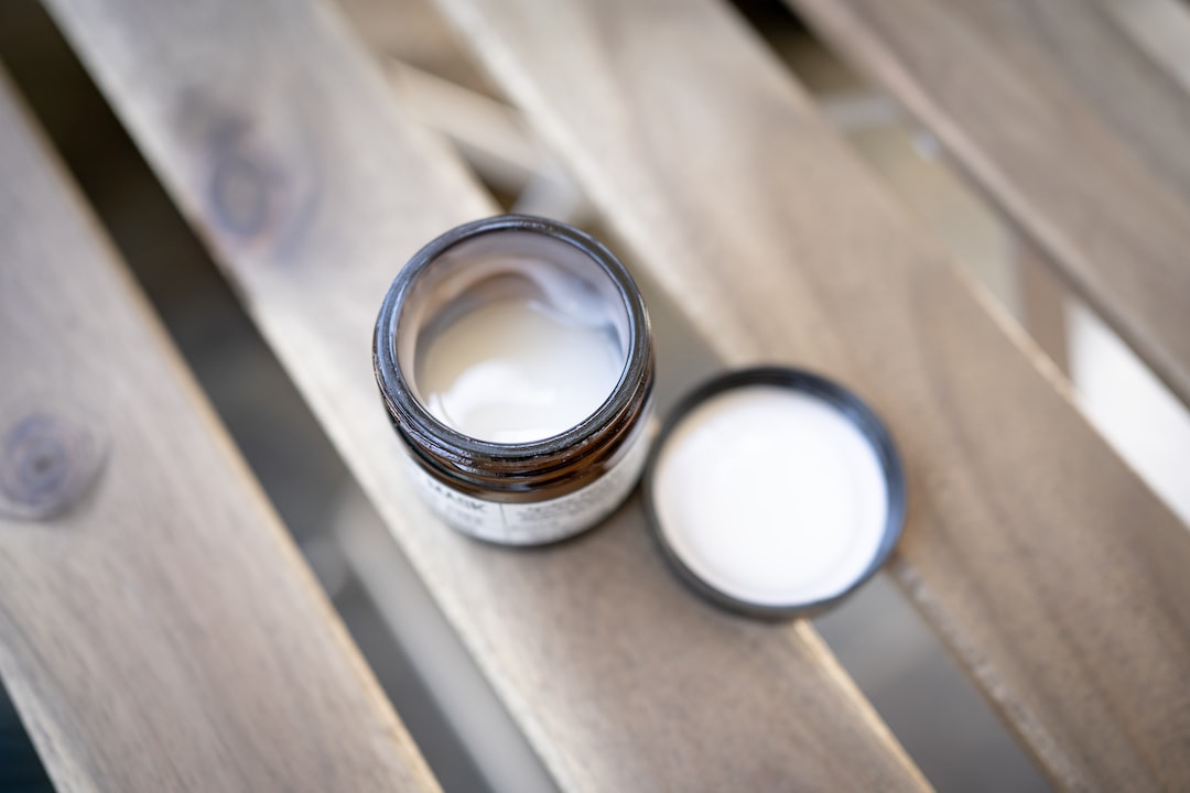 Open amber glass jar of natural white moisturizing cream on a wooden slatted surface